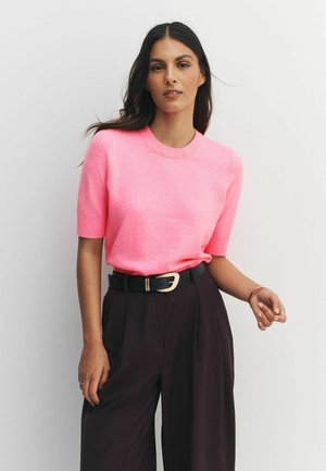 Fuchsiafarbenes Kurzarmpullover mit rundem Ausschnitt, kombiniert mit hoch taillierten dunklen Hosen und einem schwarzen Gürtel mit goldfarbenem Akzent.