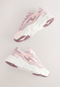 Paire de baskets épaisses roses et lavande avec des semelles blanches épaisses flottant sur un fond neutre.