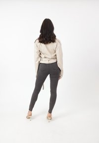 Giacca in finta pelle beige con vestibilità ampia, abbinata a jeans skinny grigio scuro e sandali con tacco beige, vista da dietro.
