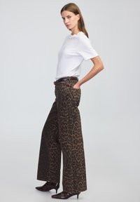 Spodnie w szerokie nogawki w gepardzi wzór w brązowym i czarnym kolorze, w połączeniu z prostą białą koszulką z krótkim rękawem i brązowymi lakierowanymi butami na obcasie w kształcie szpica.