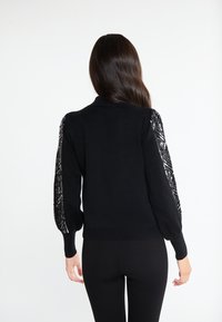 Maglione nero con maniche testurizzate e a motivo. Design aderente, polsini e orlo a coste, tessuto morbido, con dettagli intricati sulle maniche.