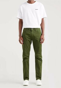 Bílá tričko s krátkým rukávem s logem Levi's, v kombinaci s olivově zelenými kalhotami a bílými teniskami, představující neformální outfit s jednoduchým designem.