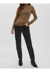 Brauner Rollkragenpullover und schwarze Jeans, mit schmaler Passform, glatter Textur und spitzen schwarzen Absatzstiefeln, die vor einem neutralen Hintergrund stehen.
