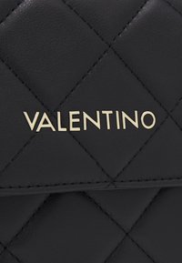 Meln�ā kvadrāta ādas rokassoma ar zelta "Valentino" logotipu. Iezīmē gludu tekstūru un dimanta rakstu uz virsmas.