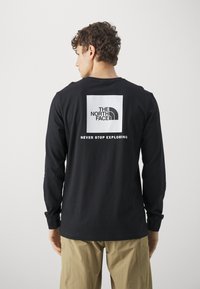 Black long-sleeve shirt made of soft cotton with a rectangular white logo featuring "THE NORTH FACE" and "NEVER STOP EXPLORING" on the back.