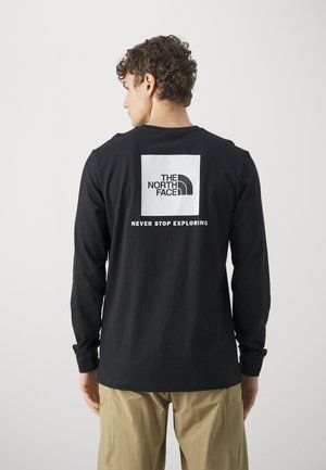 Black long-sleeve shirt made of soft cotton with a rectangular white logo featuring "THE NORTH FACE" and "NEVER STOP EXPLORING" on the back.