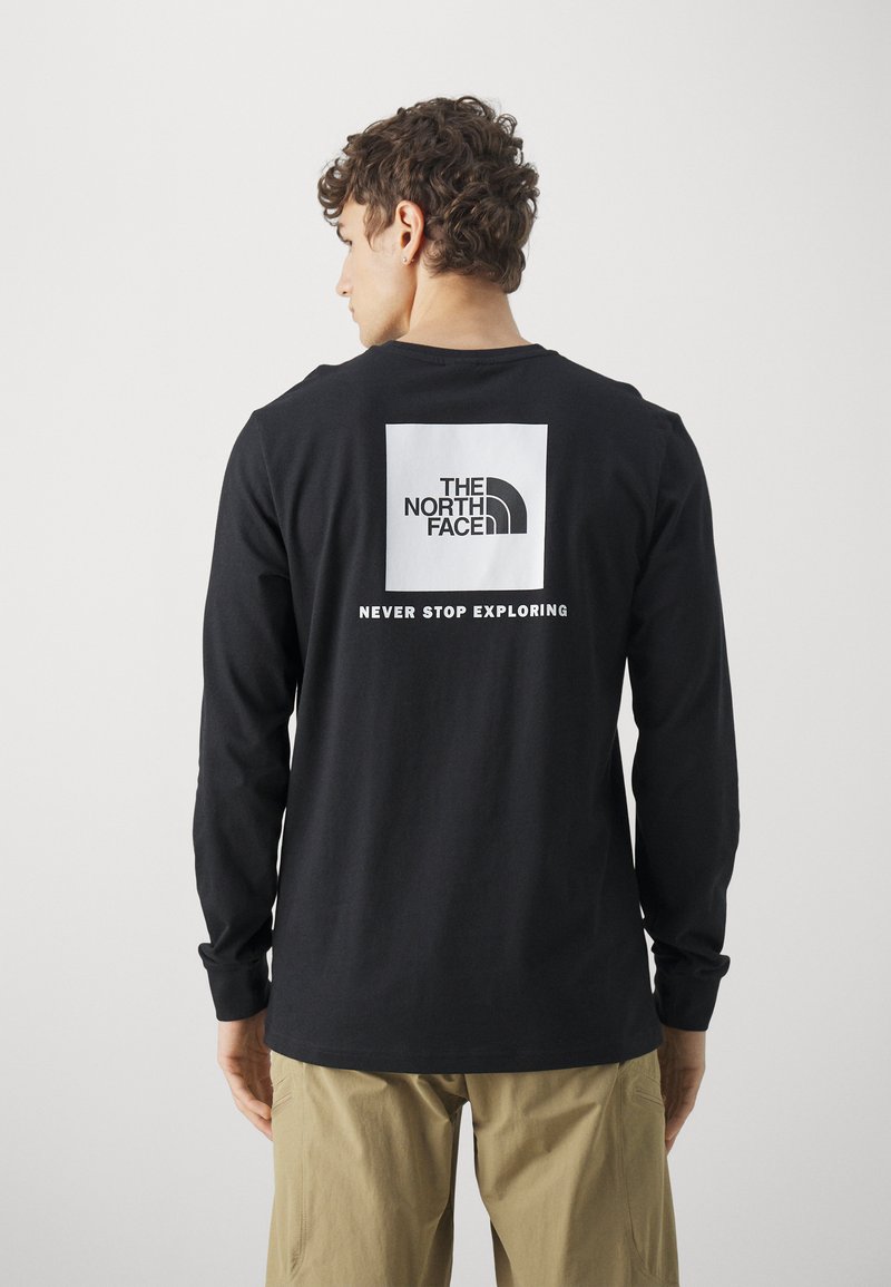 Black long-sleeve shirt made of soft cotton with a rectangular white logo featuring "THE NORTH FACE" and "NEVER STOP EXPLORING" on the back.