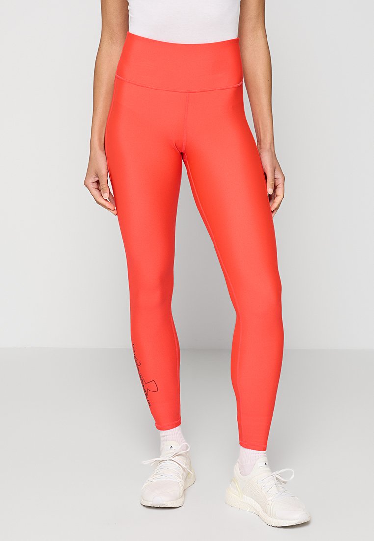 Leggings de color coral brillante, hechos de un material elástico, con una cintura alta y un detalle gráfico lateral. Llevados con zapatillas deportivas blancas.