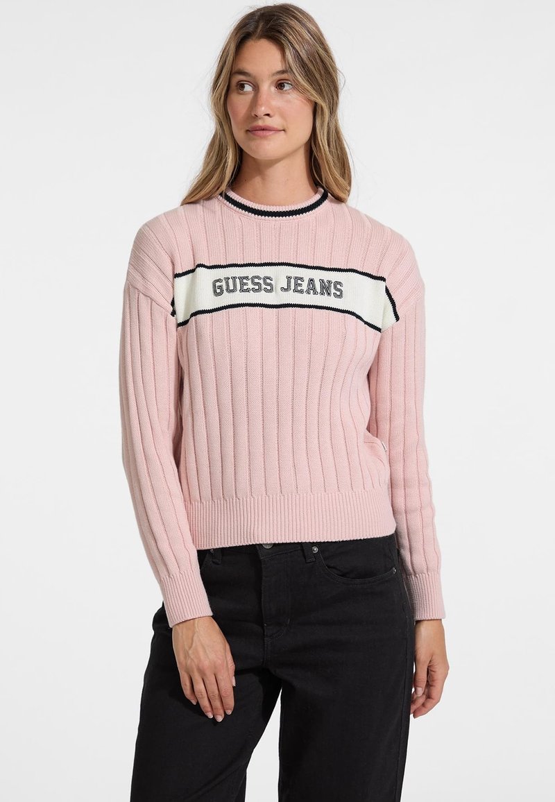 Ljusrosa ribbad tröja med ett vitt och svart randigt band som har texten "GUESS JEANS". Långa ärmar och rund halsringning.