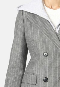 Abrigo gris a rayas con diseño de doble botonadura, botones negros y una capucha de punto gris claro unida al cuello.
