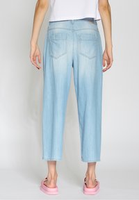 Ljusblå denimbyxor med en avslappnad passform, med raka ben, två bakfickor och synlig sömnad. Bärs med rosa sandaler.