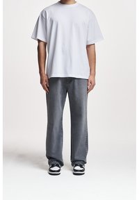 Bílé oversized tričko s krátkými rukávy, kombinované se šedými volnými džínami a černo-bílými teniskami; minimalistický design, měkká látka.