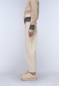 Beige knit sweater with a textured pattern and multicolor ribbed cuffs, paired with straight-leg cream pants and beige fuzzy slip-on shoes.