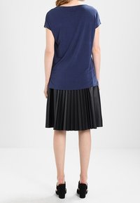 Námořnická modrá halenka s krátkým rukávem v kombinaci s černou skládací sukní. Halenka je měkká s volným střihem a sukně má vertikální sklady.