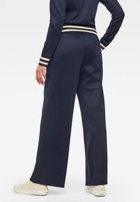 Marinblå vida byxor med en mjuk textur, med ett midjeband i vit och olivgrön randig design. Bakfickor är synliga.