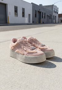 Paire de baskets compensées roses avec des détails en fourrure texturée placées sur un trottoir en béton urbain à la lumière du jour.