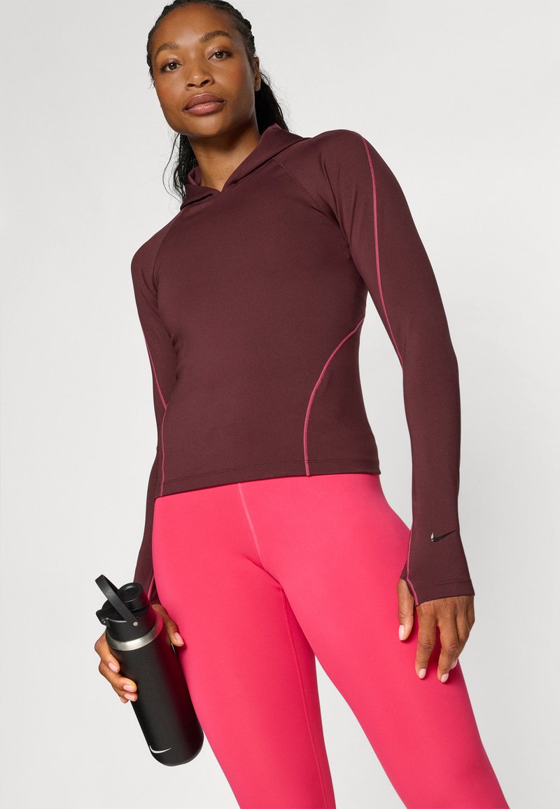 Maroon Langarm-Hoodie mit pinken Akzenten, kombiniert mit enganliegenden pinken Leggings. Eine schwarze Wasserflasche mit silbernem Deckel wird in der rechten Hand gehalten.