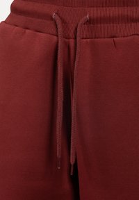 Burgunderfarbene Sweatpants aus weichem Stoff, mit einem gerippten Bund und Kordeln zur Anpassung. Glatte Textur ohne sichtbare Muster.