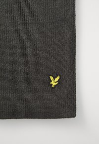 Bufanda de punto gris oscuro con textura acanalada, que presenta un pequeño logotipo de águila bordado en amarillo en la esquina inferior.