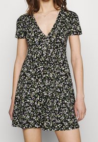 Czarna sukienka w kwiaty z głębokim dekoltem w serek, krótkimi rękawami i rozkloszowanym dołem. Charakteryzuje się małymi białymi i zielonymi kwiatkami na ciemnym tle.