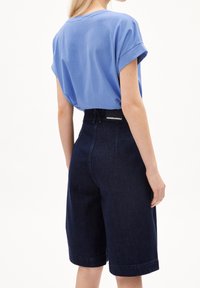 Jasnoniebieski t-shirt z krótkim rękawem w połączeniu z ciemnymi, wysokim stanem, szortami z denimu o prostym kroju i podwiniętych brzegach.