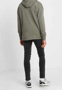Grauer Kapuzenpullover mit Kapuze, lässige Passform, kombiniert mit schwarzen Skinny-Jeans. Die Sneakers haben ein Schwarz-Grau-Farbdesign mit weißen Akzenten.