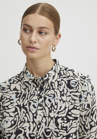 Overhemd met knoopsluiting, voorzien van een zwart en crème abstract patroontje met blauwe accenten, ontworpen met een kraag en een gladde textuur. Zwarte knopen zichtbaar.