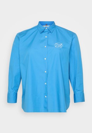 Light blue long-sleeve button-up shirt, featuring a classic collar, white embroidered logo, and front-button closure with subtle sheen.