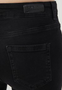 Vaqueros de denim negro con una textura suave, un único bolsillo trasero y una etiqueta de cuero de marca en la cintura.