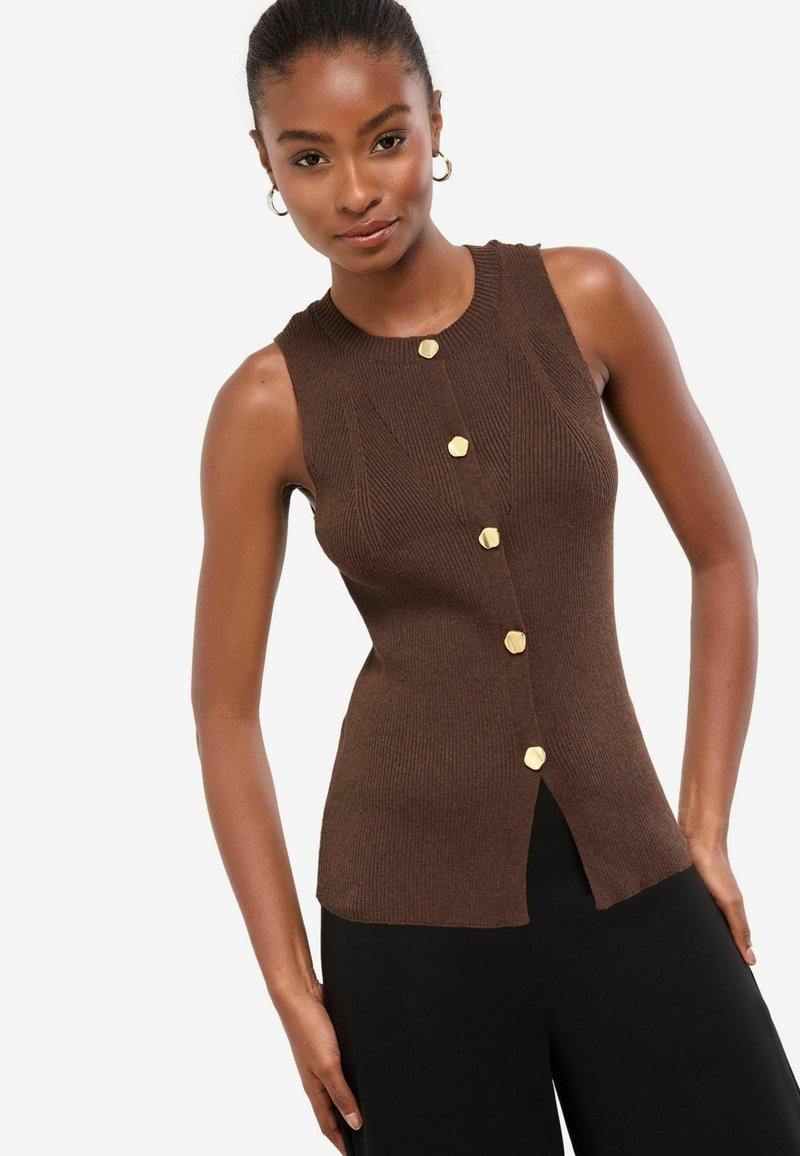 Brown ribbed knit sleeveless top featuring a round neckline, gold hexagonal buttons, and a side slit, paired with black pants.