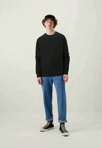 Long-sleeve black t-shirt paired with light blue ribbed pants and black high-top sneakers. Model wears a black cap. Simple, casual outfit.