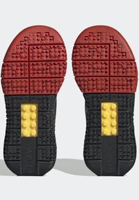 Sko sulor med ett texturerat mönster av röd gummi, med gula och svarta accenter. Ytan har blockliknande indenter för grepp.