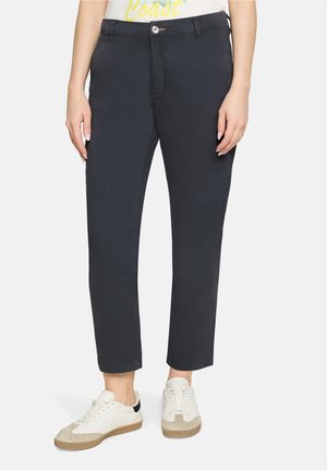 Ciemnoniebieskie spodnie o dopasowanym kroju, wykonane z bawełny, z talią o średnim stanie, zapinane z przodu na guzik, z podwiniętymi nogawkami, w połączeniu z białymi trampkami.