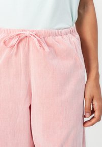 Pantaloni in velluto a coste rosa chiaro con righe verticali, dotati di vita elastica, chiusura con cordino e tasche laterali.