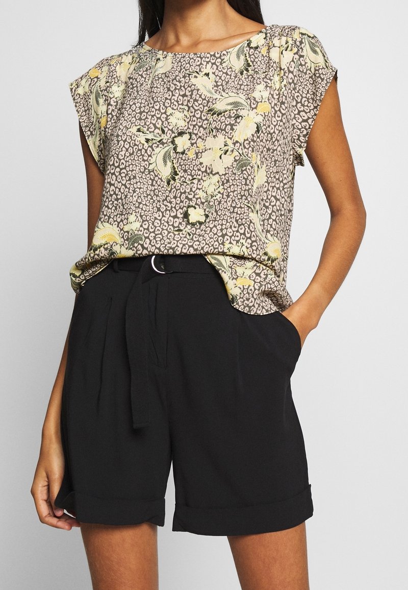 Blus med blommönster i beige, gult och grönt, med korta ärmar. Matchad med högmidjade svarta shorts med knytskärp.