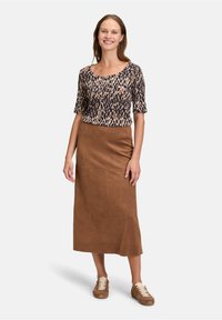 Haut à manches courtes avec imprimé animal dans des tons sombres, associé à une jupe midi en daim marron et des chaussures à lacets marron clair.