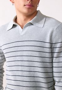 Hellgrauer Strickpullover mit einem kragenförmigen Design. Besitzt marineblaue horizontale Streifen und einen strukturierten Stoff. Kurze Ärmel mit lockerer Passform.