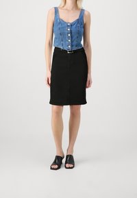 Top de denim recortado con botones en la parte delantera, combinado con una falda de denim negra de longitud media. Los accesorios incluyen mule negros de tacón abierto.