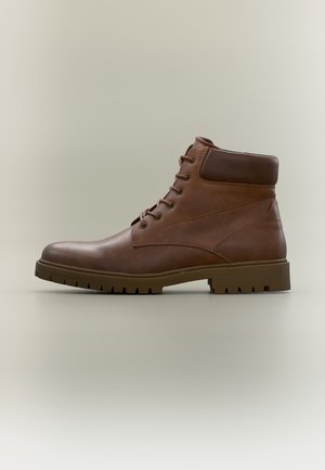 Bottine marron en cuir avec lacets sur le devant, col rembourré et semelle épaisse crantée, vue de côté sur fond neutre.