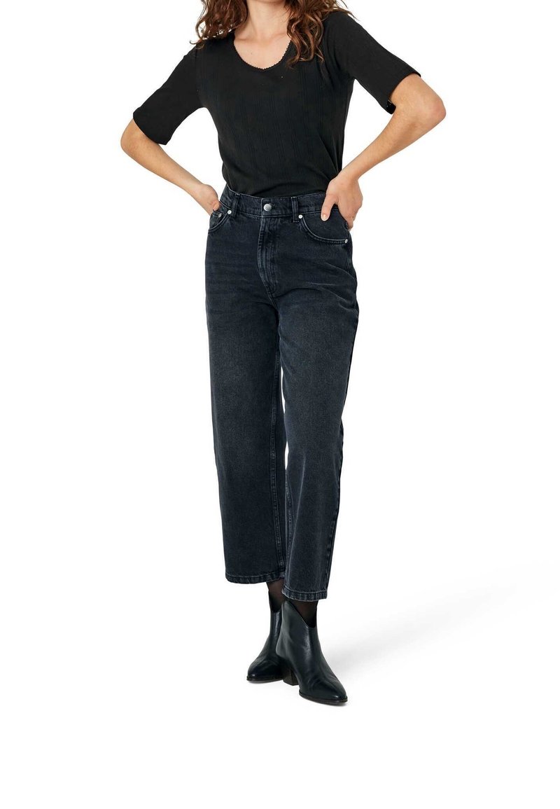 Jeans denim gelap berpinggang tinggi dengan potongan lurus, dilengkapi dengan kantong depan dan ritsleting. Dipadukan dengan atasan hitam yang pas dan sepatu bot pergelangan kaki.