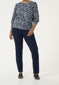 Blue zebra-striped blouse with three-quarter sleeves, paired with dark blue jeans and black heeled mules. Smooth texture throughout.
