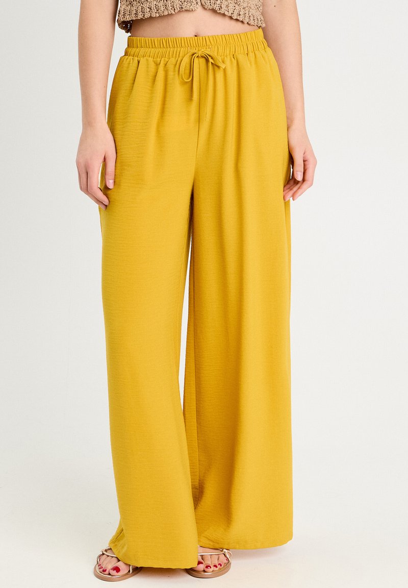 Weite gelbe Hose aus strukturiertem Stoff mit elastischem Bund. Mit einem Kordelzug für eine anpassbare Passform. Lässiges und atmungsaktives Design.