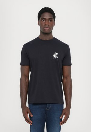 Black short-sleeve t-shirt with a round neck, featuring a white logo on the left chest. Paired with blue denim jeans.