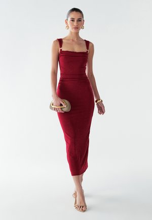 Rode aansluitende midi-jurk met gerimpelde textuur, vierkante halslijn en brede bandjes. Gepaard met een beige clutch en sandaaltjes met bandjes.
