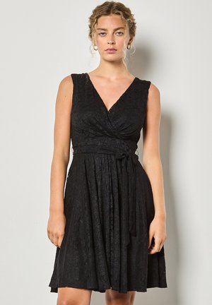 Vestido negro ajustado con escote en V, sin mangas, de tela texturizada y detalle de cintura anudada, que cae por encima de la rodilla.