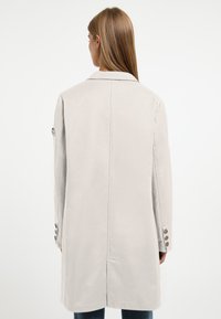 Lichtgrijze jas met een rechte snit, voorzien van een achterste split, een reverskraag en accentueringen met drie knopen op de mouwen. Gladde stofstructuur.