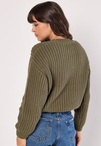 Olijfgroene gebreide trui met een textuurpatroon, ronde halslijn en verlaagde schouders, gecombineerd met hooggesneden blauwe jeans.