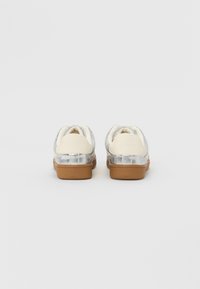 Sneaker in pelle argento con dettagli bianchi e suola in gomma marrone. Caratterizzati da punta rotonda e tallone rialzato per maggiore supporto.