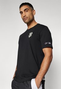 Svart bomulls t-skjorte med et lite hvitt og gull logo på brystet, med Champion-logo på ermene og rund halsdesign.