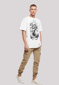 Hvit t-skjorte med kort erme med trykk i svart. Kombinert med beige cargo-bukser og hvite sneakers. Enkel, uformell antrekk.
